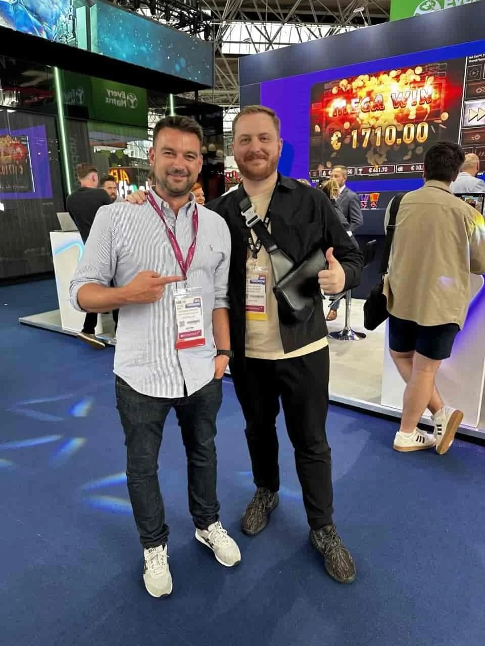 Alex and Dmitry Belianin posing for a photo in front of a ‘MEGA WIN’ screen from a slot machine game