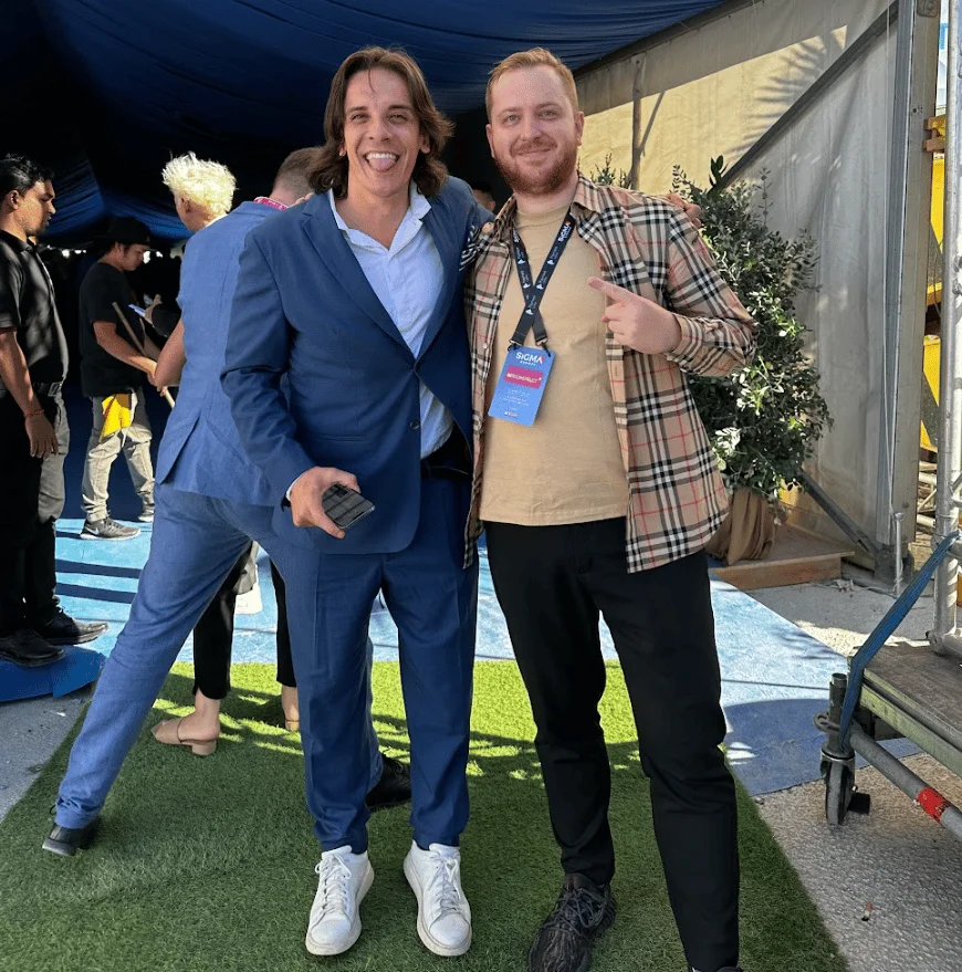 Two men posing for a photo at an event, one of whom is Dmitry Belianin; one is wearing a suit, the other a plaid shirt, both with event badges
